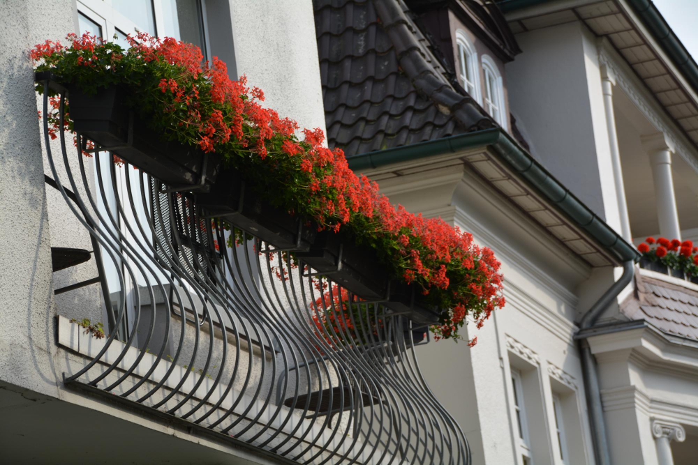 Balkon ozdobiony kolorowymi kwiatami w doniczkach, otoczony zielonymi roślinami.
