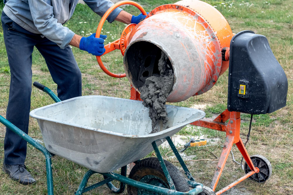 Mężczyzna miesza cement w taczce na budowie.