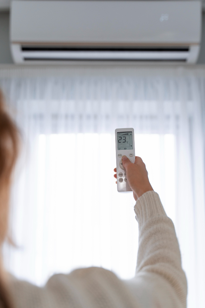 Kobieta trzymająca pilot w ręku, stojąca przed klimatyzatorem.